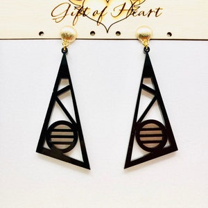 May include: A pair of black geometric triangle earrings with a gold circle design in the center. The earrings are hanging from gold posts.