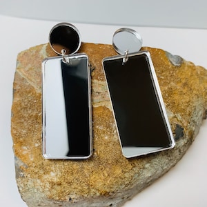 May include: A pair of silver earrings with rectangular mirror-like surfaces. The earrings have a round silver top.