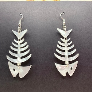 May include: A pair of white fish bone earrings with silver hooks. The earrings are made of a translucent material that resembles mother of pearl.