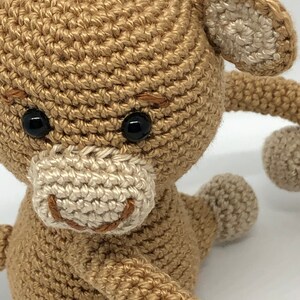 May include: A crocheted monkey toy with brown fur, white ears, and a white face. The monkey has black eyes and a brown stitched smile.