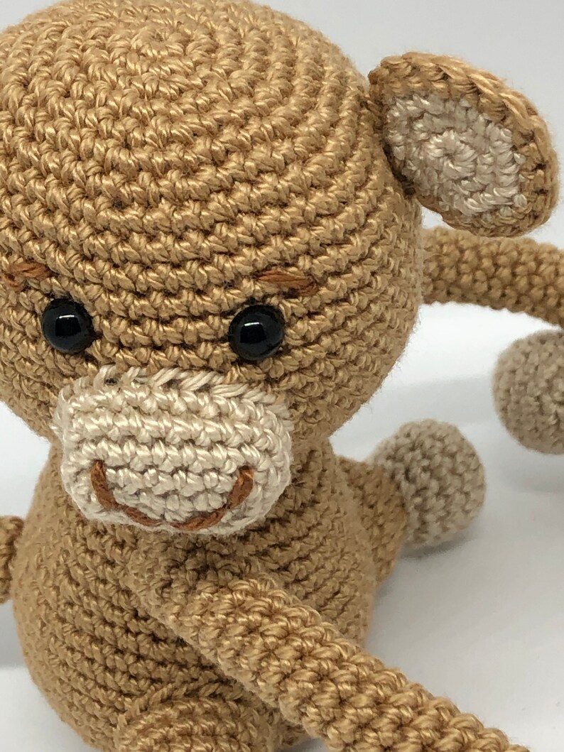 May include: A crocheted monkey toy with brown fur, white ears, and a white face. The monkey has black eyes and a brown stitched smile.