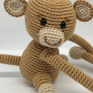 May include: A crocheted brown monkey toy with white ears and feet. The monkey has black eyes and a stitched smile.