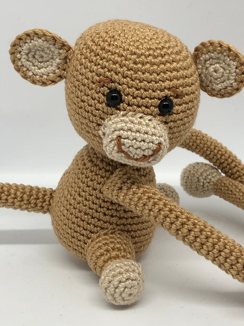 May include: A crocheted brown monkey toy with white ears and feet. The monkey has black eyes and a stitched smile.