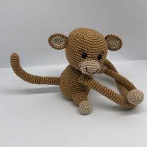 May include: A crocheted brown monkey toy with a long tail and white accents on the ears, nose, and feet.