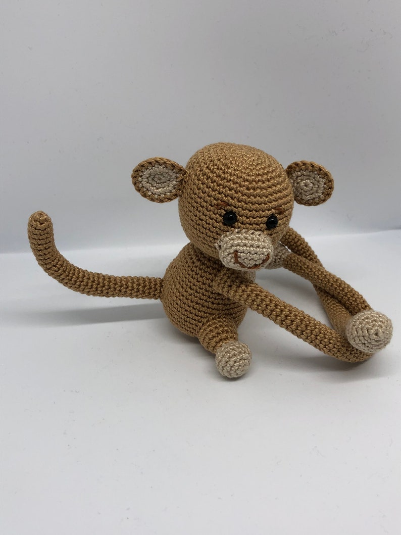 May include: A crocheted brown monkey toy with a long tail and white accents on the ears, nose, and feet.
