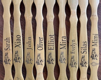 May include: Ten wooden back scratchers with personalized names, including Sarah, Xiao, John, Oliver, Elliot, Mira, Evelyn, Silas, and Mimi. Each scratcher features a fish graphic and the logo "Grand View - Lodge".