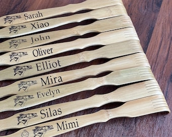 May include: A set of ten wooden back scratchers with personalized names, including Sarah, Xiao, John, Oliver, Elliot, Mira, Evelyn, Silas, and Mimi. Each scratcher features a small fish design and a unique name.
