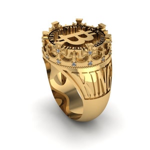 Könnte beinhalten: Ein goldener Ring mit einem Kronendesign, das ein Bitcoin-Symbol und das Wort "KING" auf der Band trägt.