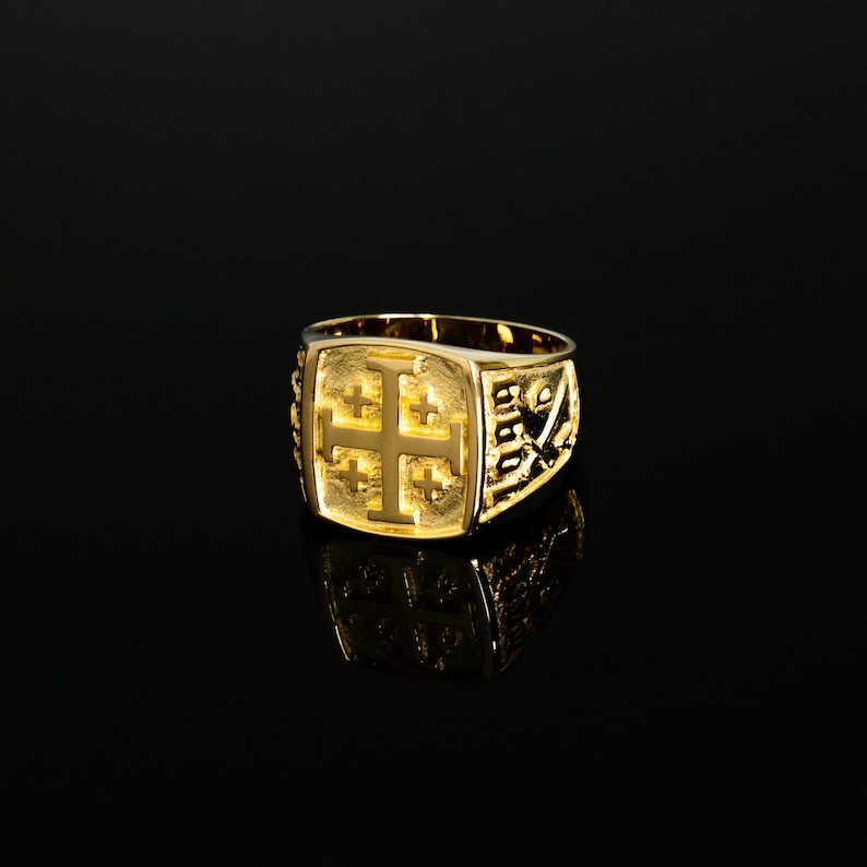 Op de afbeelding: Een gouden ring met een reli&euml;f van een kruis. Het kruis is omgeven door een decoratieve rand.