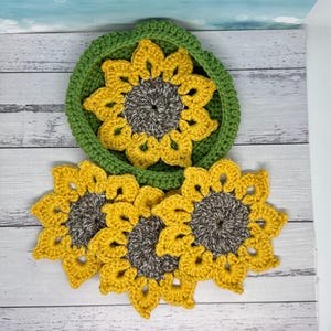 May include: Four crocheted sunflower coasters in yellow and brown with a green crocheted coaster in the center.