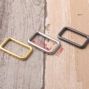 Peut inclure: Trois anneaux en D métalliques en or, argent et noir. Les anneaux sont rectangulaires et mesurent 30 mm sur 16 mm.