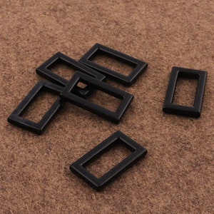 Pode incluir: Seis fivelas deslizantes retangulares de metal preto. As fivelas medem aproximadamente 2,5 cm de comprimento e 1,2 cm de largura.