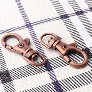 May include: Two antique copper-toned metal swivel clasps or hooks. The clasps are on a white and black checkered background.