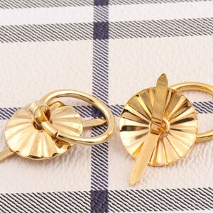 Op de afbeelding: Twee messingkleurige metalen ladegrepen met een decoratief, geribbeld ontwerp. Elke greep heeft een ringvormige handgreep en een puntig, decoratief accent.