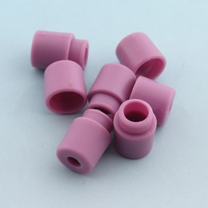 May include: A group of six pink ceramic caps, some stacked on top of each other. The caps are cylindrical in shape with a slightly rounded top and a smooth surface.