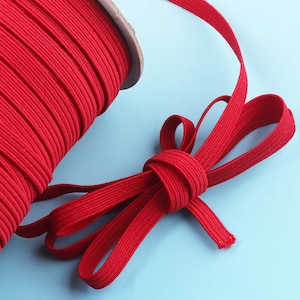 May include: A spool of bright red elastic cord with a length of cord tied into a bow shape.