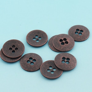 May include: A group of eight copper-colored buttons with four holes each. The buttons are arranged in a semi-circle on a light blue background.