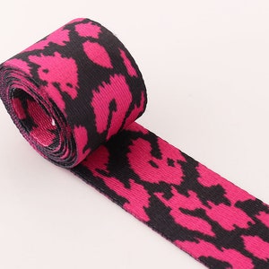 May include: Pink and black patterned webbing ribbon. The ribbon has a black and pink animal print design.
