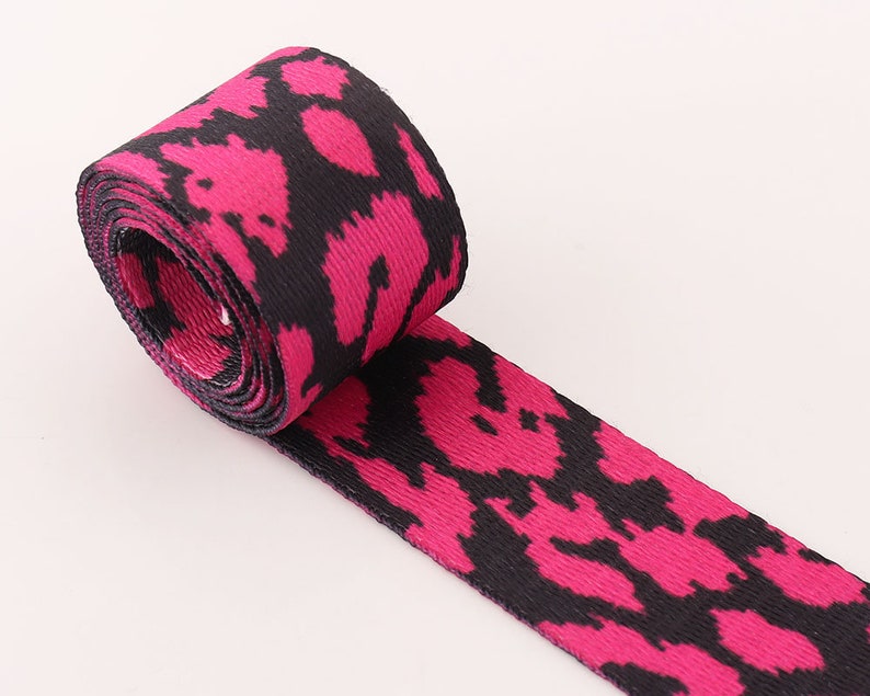 May include: Pink and black patterned webbing ribbon. The ribbon has a black and pink animal print design.