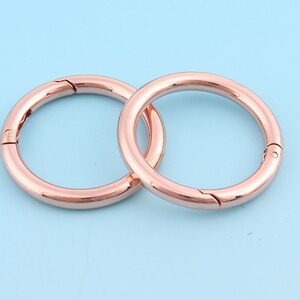 May include: Two rose gold metal key rings with a swivel clasp. The rings are interlocked.