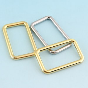 May include: Three metal rings, two gold and one silver, are stacked on top of each other. The rings are all rectangular in shape and have rounded edges.