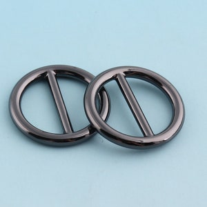 Puede incluir: Dos anillos de metal negro con una barra central. Los anillos son lisos y brillantes.