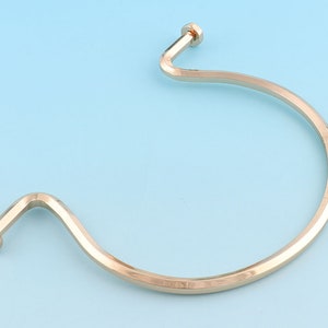 May include: A gold-toned metal bangle bracelet with a curved, open design. The bracelet has a smooth, polished finish.