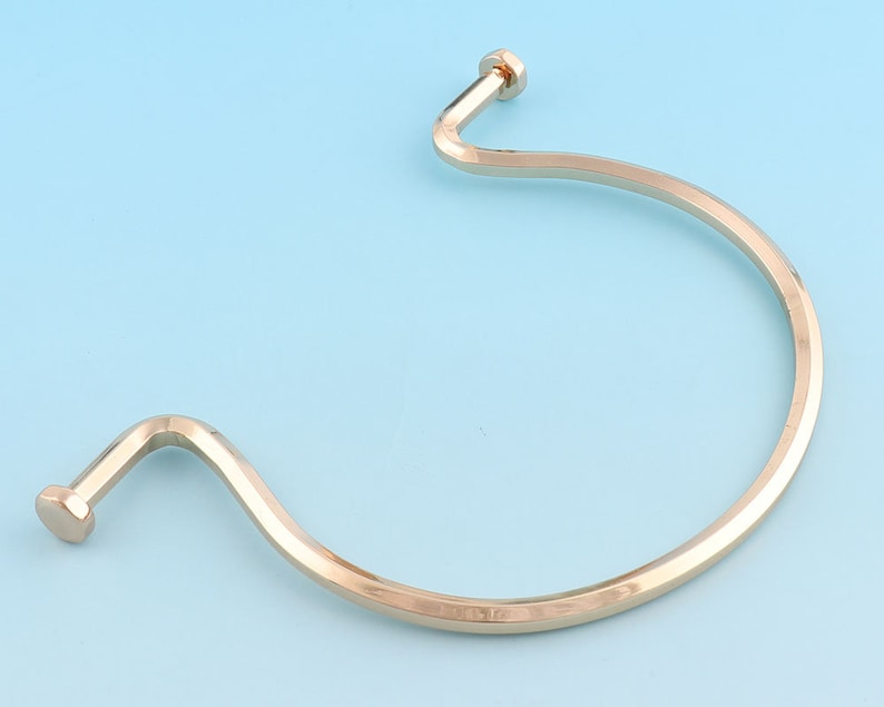 May include: A gold-toned metal bangle bracelet with a curved, open design. The bracelet has a smooth, polished finish.