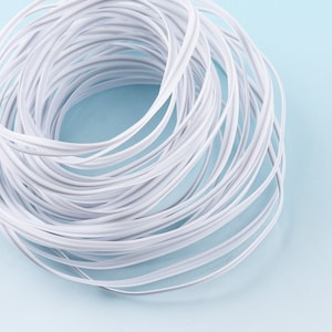 Könnte beinhalten: Nahaufnahme eines weißen Kunststoffkabels, das zu einem Kreis gewickelt ist. Das Kabel ist flexibel und hat eine glatte Oberfläche.