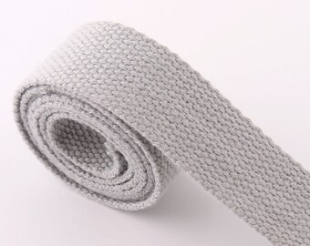 Puede incluir: Una longitud enrollada de tela tejida gris claro. El material parece ser un algodón resistente o un textil similar, con un tejido texturizado visible. La tela está enrollada en espiral, mostrando el borde y la textura del material.