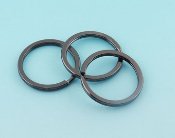 Könnte beinhalten: Drei ineinander verschlungene schwarze Schlüsselringe aus Metall. Die Ringe sind glatt und glänzend.