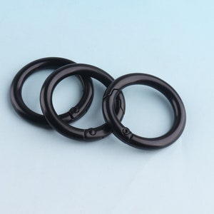 Può includere: Tre portachiavi in metallo nero con chiusura a molla. Gli anelli sono impilati, con l'anello più grande in basso e l'anello più piccolo in alto.