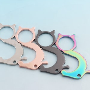 May include: Four cat-shaped door openers in different colors: silver, rose gold, black, and iridescent. The openers have a loop on one end and a hook on the other.