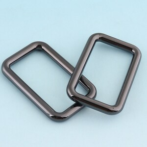 May include: Two black metal D-rings, one overlapping the other. The rings are smooth and have a shiny finish.