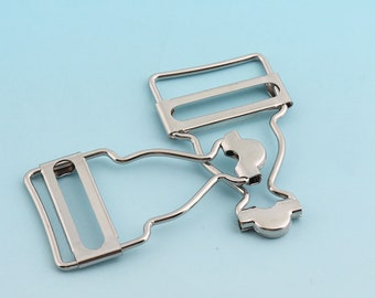 May include: Silver metal slider buckle for clothing. The buckle has two parts, one with a rectangular loop and the other with a curved shape.