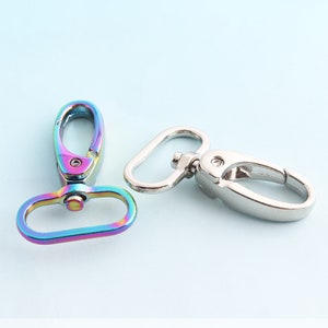 May include: Two metal clasps, one silver and one iridescent rainbow. The silver clasp is a simple oval ring with a hook. The rainbow clasp has a more complex design with a hook and a D-ring.