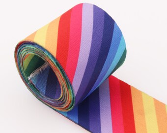 Könnte beinhalten: Ein zusammengerolltes, regenbogenfarbenes, gestreiftes Gummiband. Das Band besteht aus einem weichen, dehnbaren Stoff und hat ein farbenfrohes Regenbogenmuster.