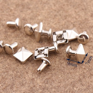 Könnte beinhalten: Silberne pyramidenförmige Nieten mit einer Basis von 9 mm und einer Höhe von 7 mm. Die Nieten haben eine spitze Oberseite und eine flache Unterseite. Sie sind ideal, um Lederwaren, Kleidung und anderen Bastelarbeiten eine dekorative Note zu verleihen.
