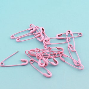 Pu&ograve; includere: Un gruppo di spille da balia rosa sparse su uno sfondo blu chiaro.