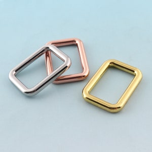 Può includere: Tre anelli metallici in diverse finiture: argento, oro rosa e oro. Gli anelli sono di forma rettangolare con angoli arrotondati.