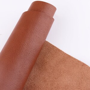 May include: A roll of brown leather with a textured surface. The leather is rolled up and the end is visible. The leather is on a white background.