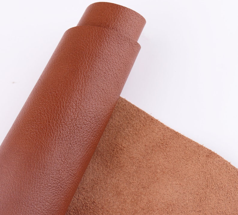 May include: A roll of brown leather with a textured surface. The leather is rolled up and the end is visible. The leather is on a white background.