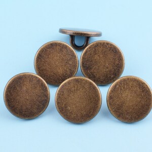 May include: Six antique gold-toned metal buttons with a smooth, slightly textured surface. The buttons are round and have a flat back.