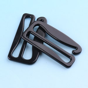 Puede incluir: Dos hebillas deslizantes de plástico negro para correas o cinturones. Las hebillas están diseñadas para ser usadas con una correa o cinturón de 25 mm de ancho.