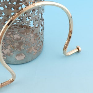 May include: Gold metal handle with a rounded top and two small, round knobs at the ends. The handle is curved and has a smooth, polished finish.