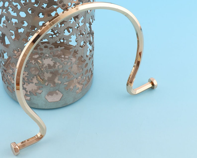 May include: Gold metal handle with a rounded top and two small, round knobs at the ends. The handle is curved and has a smooth, polished finish.