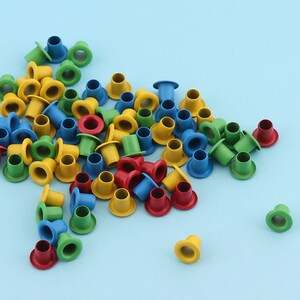 May include: Assortment of colorful metal eyelets in blue, yellow, green, and red. The eyelets are small and round with a hole in the center.