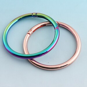 May include: Two metal rings, one iridescent and one rose gold, are interlocked. The iridescent ring has a rainbow finish.