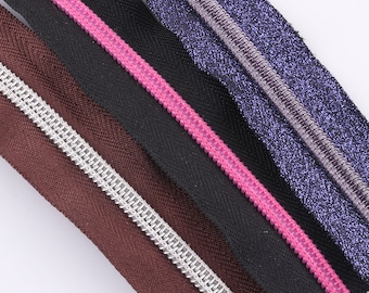 Puede incluir: Cinco cintas de cremallera de diferentes colores, incluyendo marrón, negro, rosa y morado. Las cintas están dispuestas horizontalmente, con la cinta marrón en la parte superior y la cinta morada en la parte inferior.