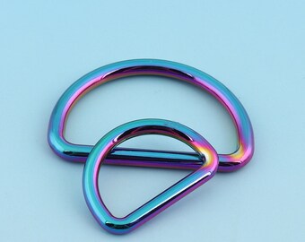 Puede incluir: Dos anillos en D de metal iridiscente, uno más grande que el otro, con un acabado arcoíris. Los anillos están apilados uno encima del otro.